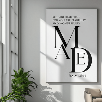 Framed artwork with text and 'MADE' design on a wall with a plant and chair in the foreground.