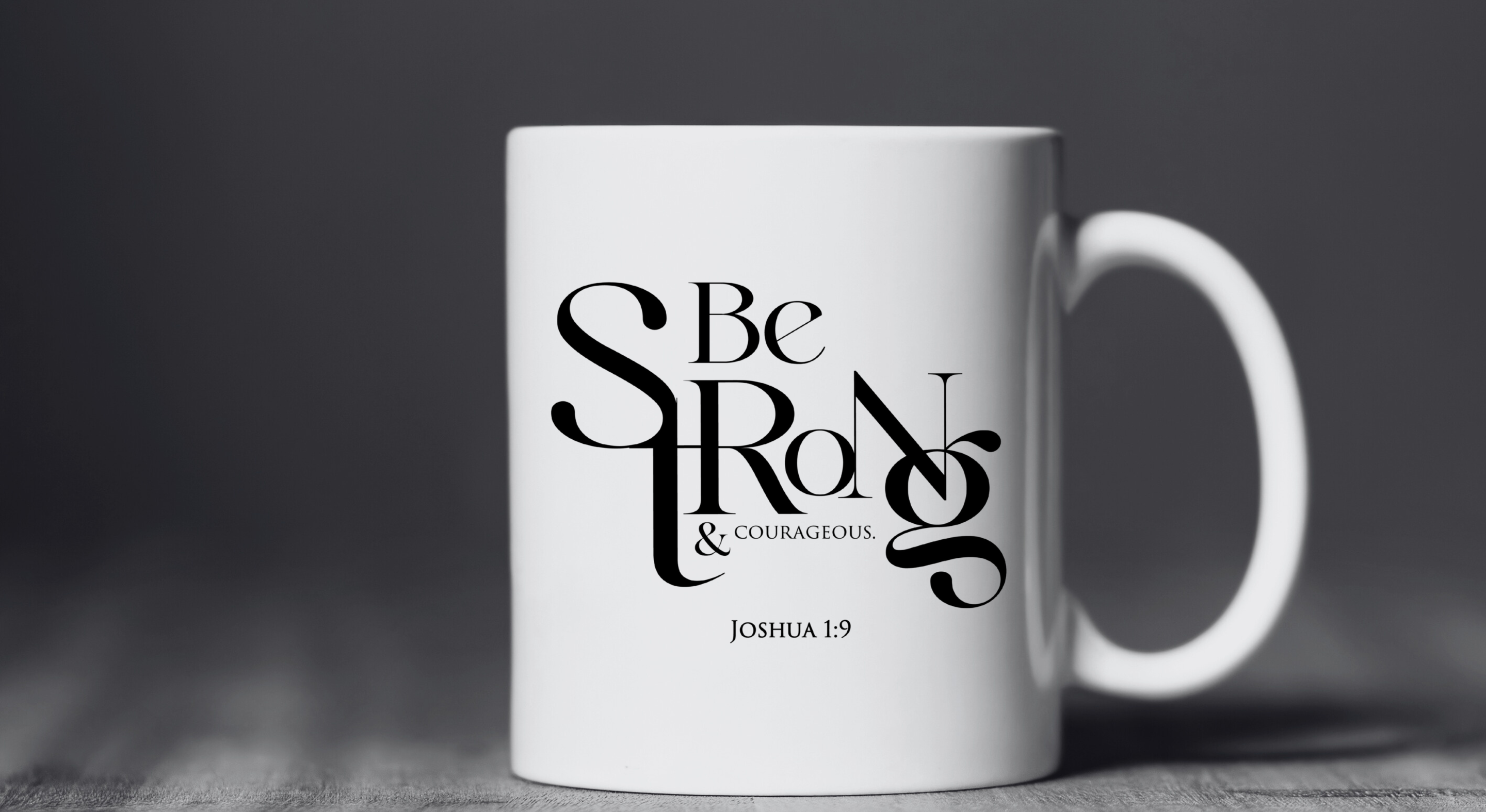 Close-up of white Christian mug with Joshua 1:9 verse – “Be Strong & Courageous” typography design