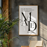 Framed artwork with text on a wall next to a plant