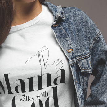 Person wearing a white t-shirt with 'This Mama Walks with God' text, paired with a denim jacket.
