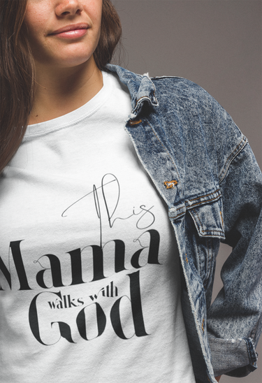 Person wearing a white t-shirt with 'This Mama Walks with God' text, paired with a denim jacket.