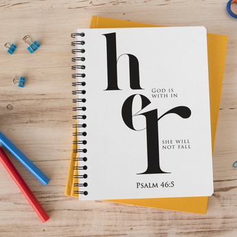 Notebook with 'God is with her, she will not fall' quote on a wooden surface with stationery items.